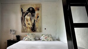 A bedroom with a large bed, two pillows with floral patterns, a nightstand with a lamp, and a painting on the wall.