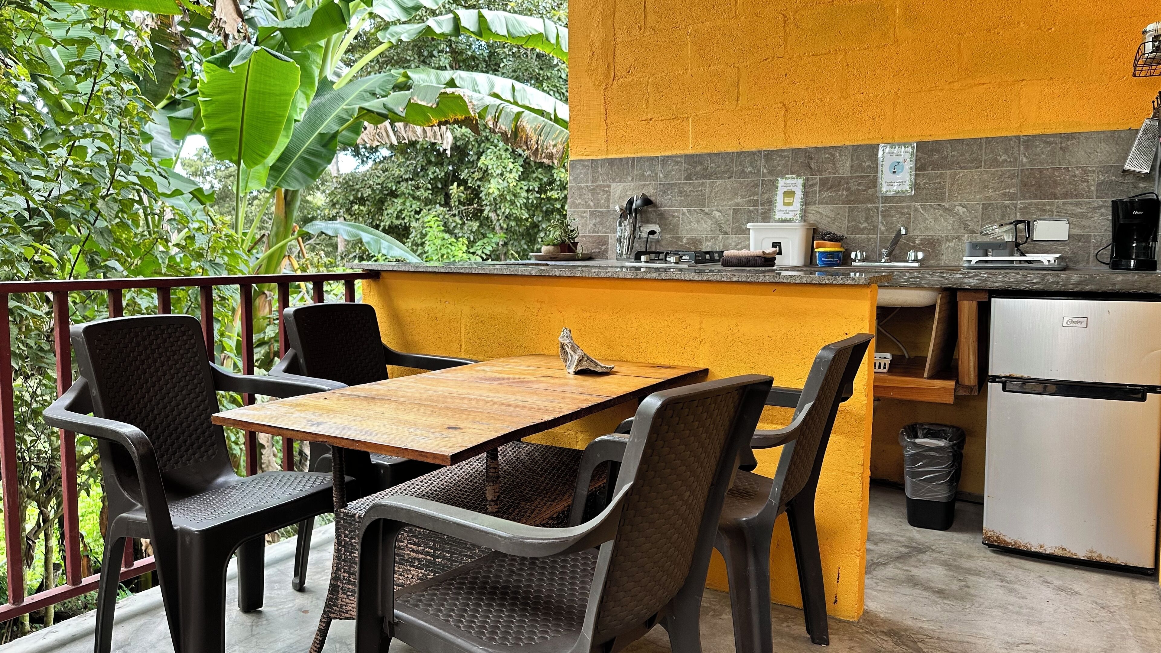 A small outdoor kitchen with a wooden table and chairs, a sink, and a refrigerator.