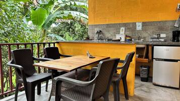 A small outdoor kitchen with a wooden table and chairs, a sink, and a refrigerator.