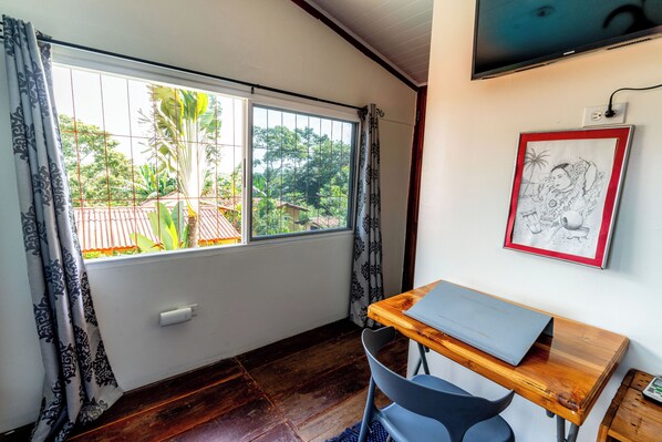 A room with a wooden desk, a chair, a TV mounted on the wall, and a window with curtains. - Close to beaches, mountains, waterfalls. Great for nomads/retreats. Quiet/rural (Panama Oeste)