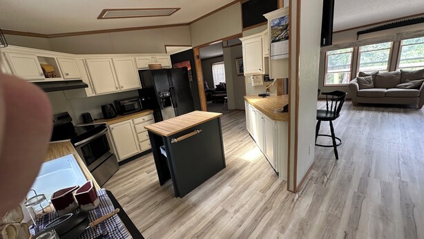 A modern kitchen with white cabinets, a black refrigerator, and a wooden island. There is a dining area with a wooden table and chairs, and a living room with a sofa and a TV. - Toots and Elmer’s Beautiful home on the Wind River (dubois)