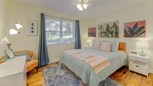 Une chambre à coucher comprenant un lit, des tables de chevet, un bureau, une chaise, un ventilateur de plafond et des œuvres d’art accrochées aux murs.