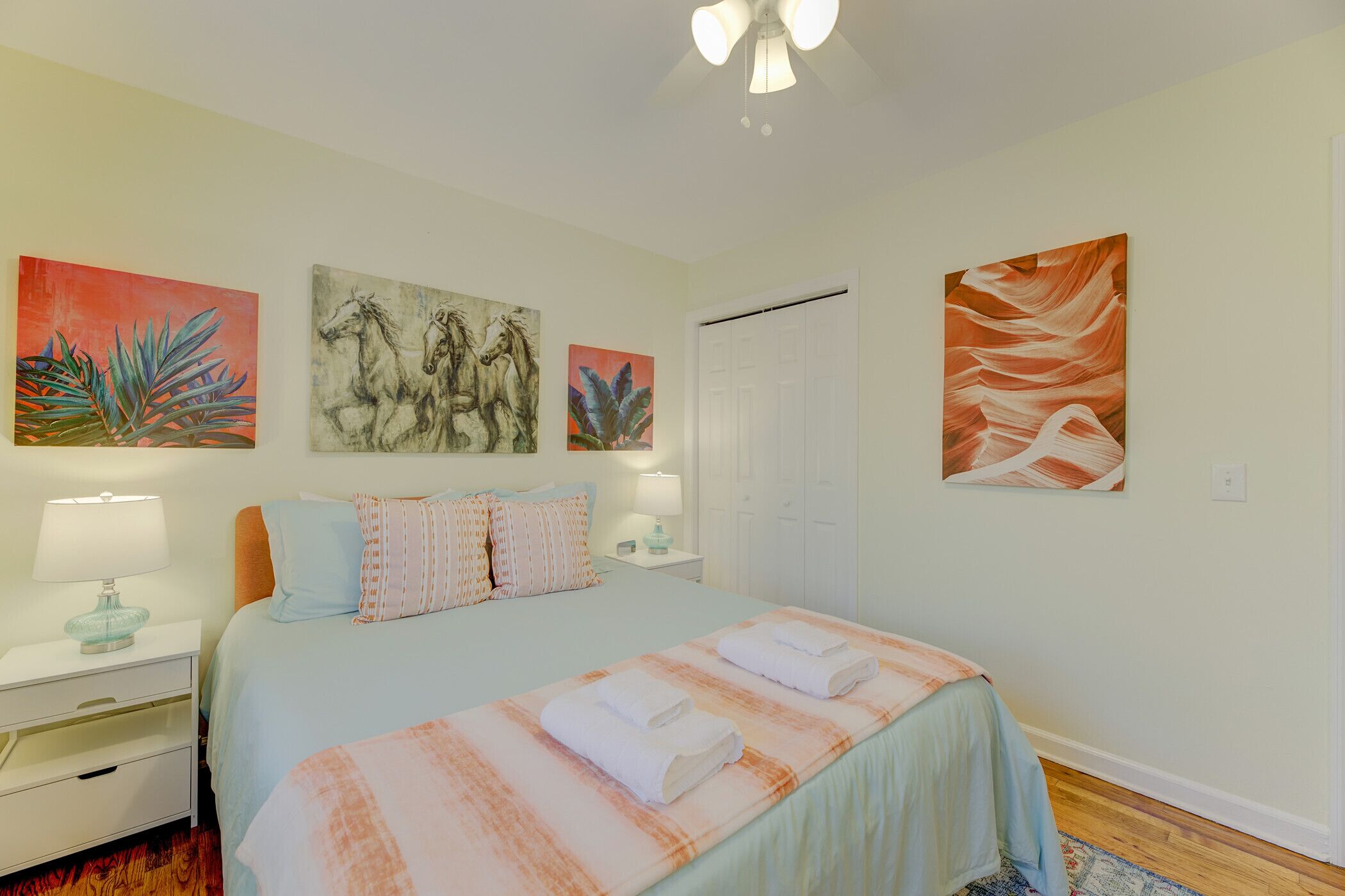 A bedroom with a bed, nightstands, a lamp, and artwork on the walls.