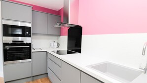 A modern kitchen with grey cabinets, a black oven, a white countertop, and a pink accent wall. - 3 The Paddock (Chathill)