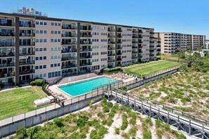 A multi-story residential building with a swimming pool, balconies, and a grassy area.
