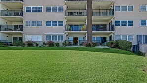 Un edificio residencial de varios pisos con balcones, un césped cuidado y un pequeño jardín.