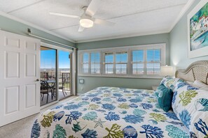 Ein Schlafzimmer mit Bett, Deckenventilator, Fenster mit Rollläden und Blick ins Freie.