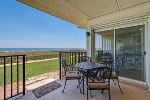 A covered patio with a table and chairs, a sliding glass door, and a view of the beach.