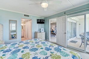A bedroom with a bed, a television, a dresser, and a sliding glass door leading to a balcony.