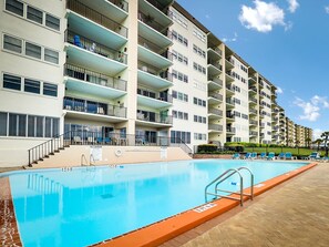 Ein mehrstöckiges Hotel mit Schwimmbad, Balkonen und blauem Himmel.