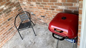 A brick wall, a window, a red grill, and a metal chair. - Very Spacious, Open Floor Plan 2 Bedroom Apt.  (Gray)