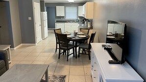 A modern kitchen with white cabinets, a dining table set for four, and a flat-screen TV on a white cabinet. - Very Spacious, Open Floor Plan 2 Bedroom Apt.  (Gray)
