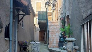 A narrow alleyway with stone paving, potted plants, and outdoor seating.