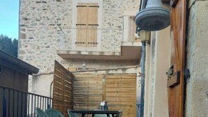 A patio area with a table and chairs, a wooden fence, and a stone building with a window and shutters in the background.