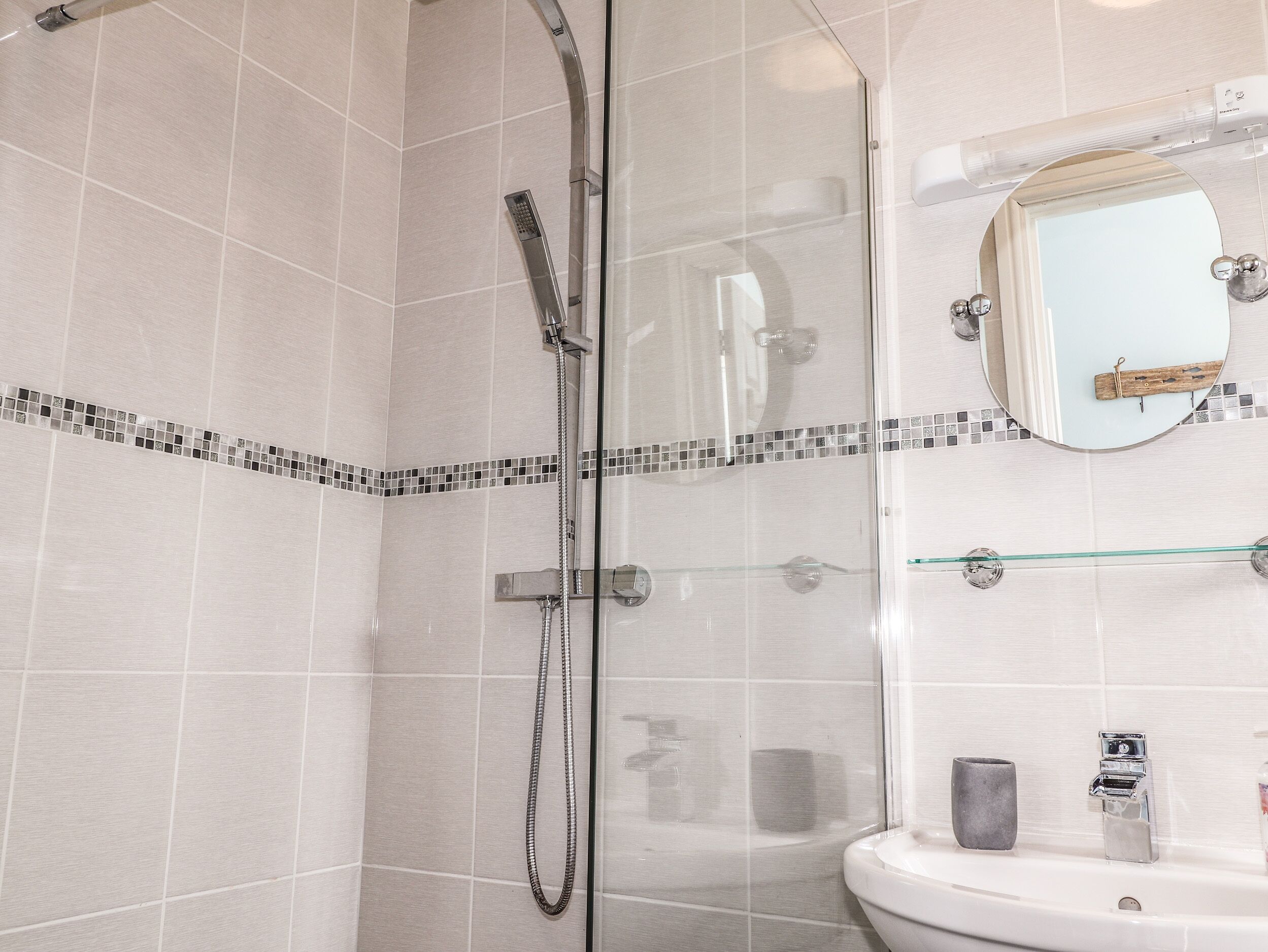 A modern bathroom with a glass-enclosed shower, a white sink, and a mirror with a wooden frame.