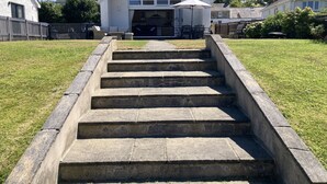 A set of stone steps leading to a house with a large window and a door, surrounded by a grassy lawn and a wooden fence. - Awel Deg, Newport (Newport)