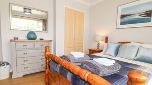 A bedroom with a wooden bed, a dresser, a mirror, a door, and a painting on the wall. - Awel Deg, Newport (Newport)