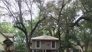 Une maison à deux étages avec un porche à l’avant, entourée d’arbres et accessible par un chemin menant à l’entrée.