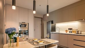 A modern kitchen with a dining area, featuring a central island, pendant lighting, and a view into the adjacent dining room. - Somerset Southbay Zhuhai (Zhuhai)