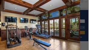 Une salle de sport équipée de matériel d’exercice, dotée de grandes fenêtres et offrant une vue sur des palmiers.