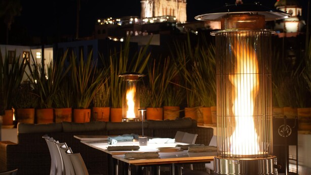 An outdoor seating area with tables and chairs, a fire feature, and a view of a cathedral in the background. - Casa 1810 Parque Hotel Boutique (San Miguel de Allende)