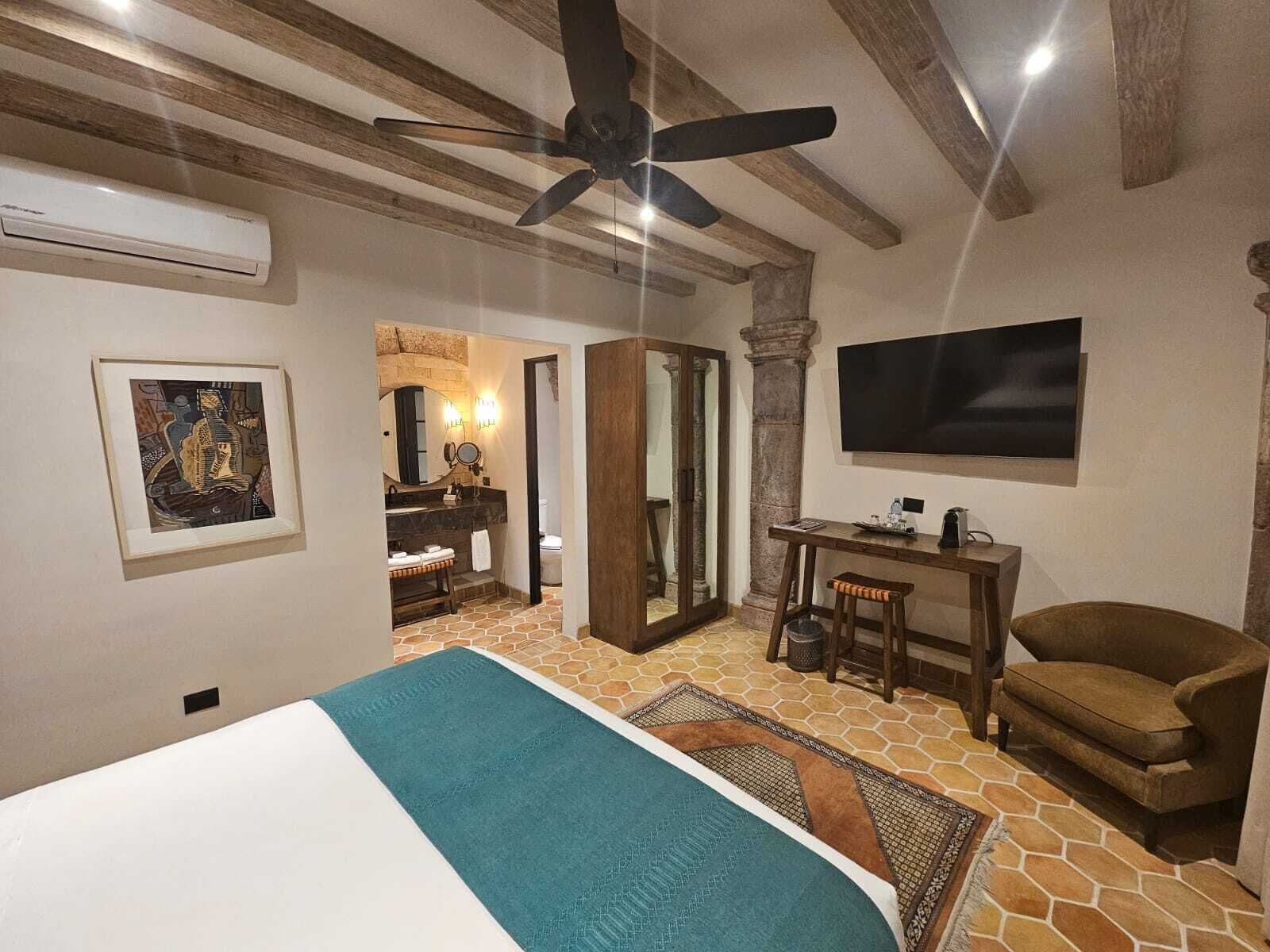 A bedroom with a bed, a ceiling fan, a TV, a desk, and a chair.