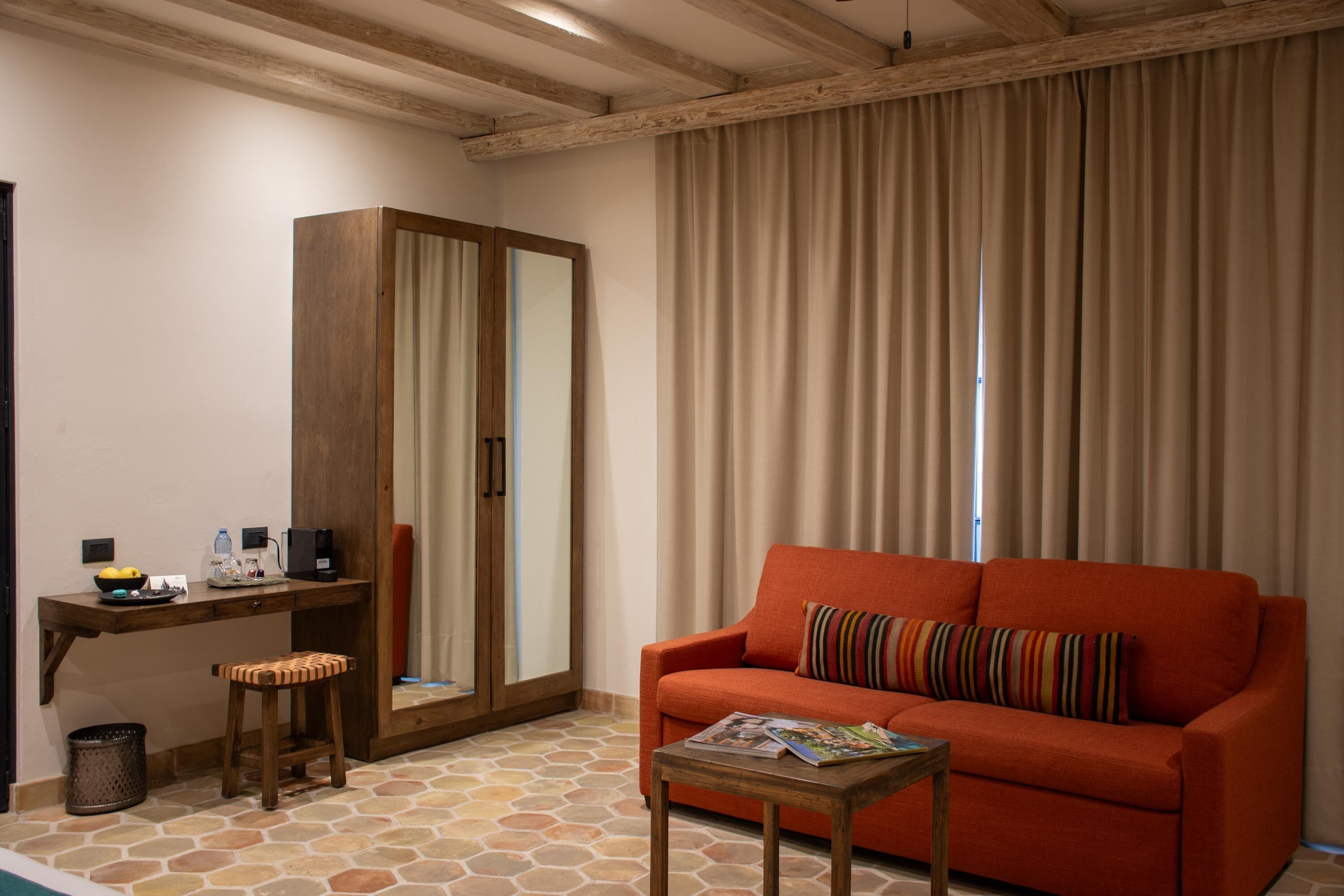 Una habitación con un escritorio de madera, un sofá rojo, un cojín a rayas y suelo de baldosas.