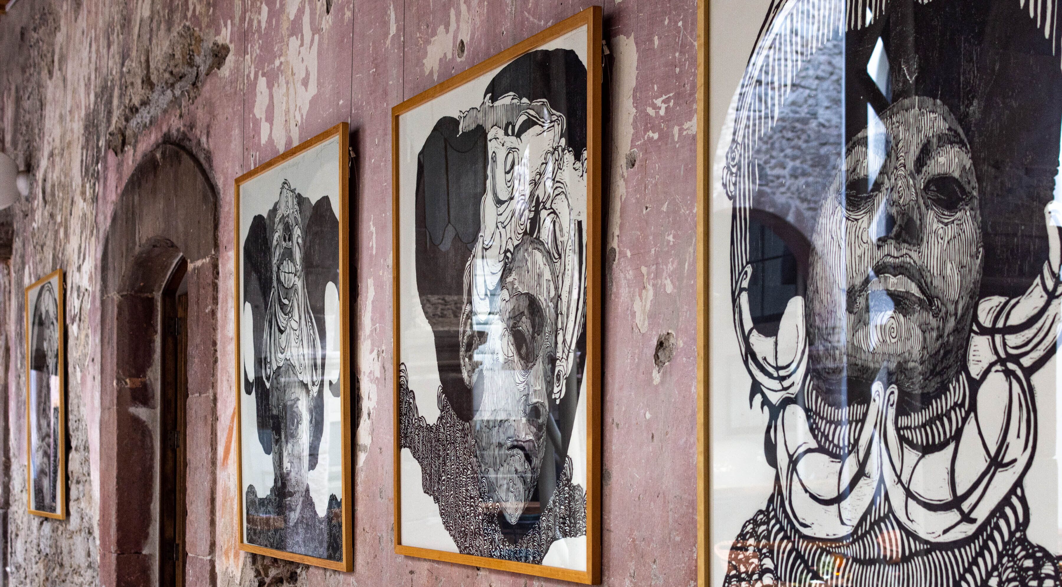 A series of framed artworks on a wall with a rustic, peeling paint finish.