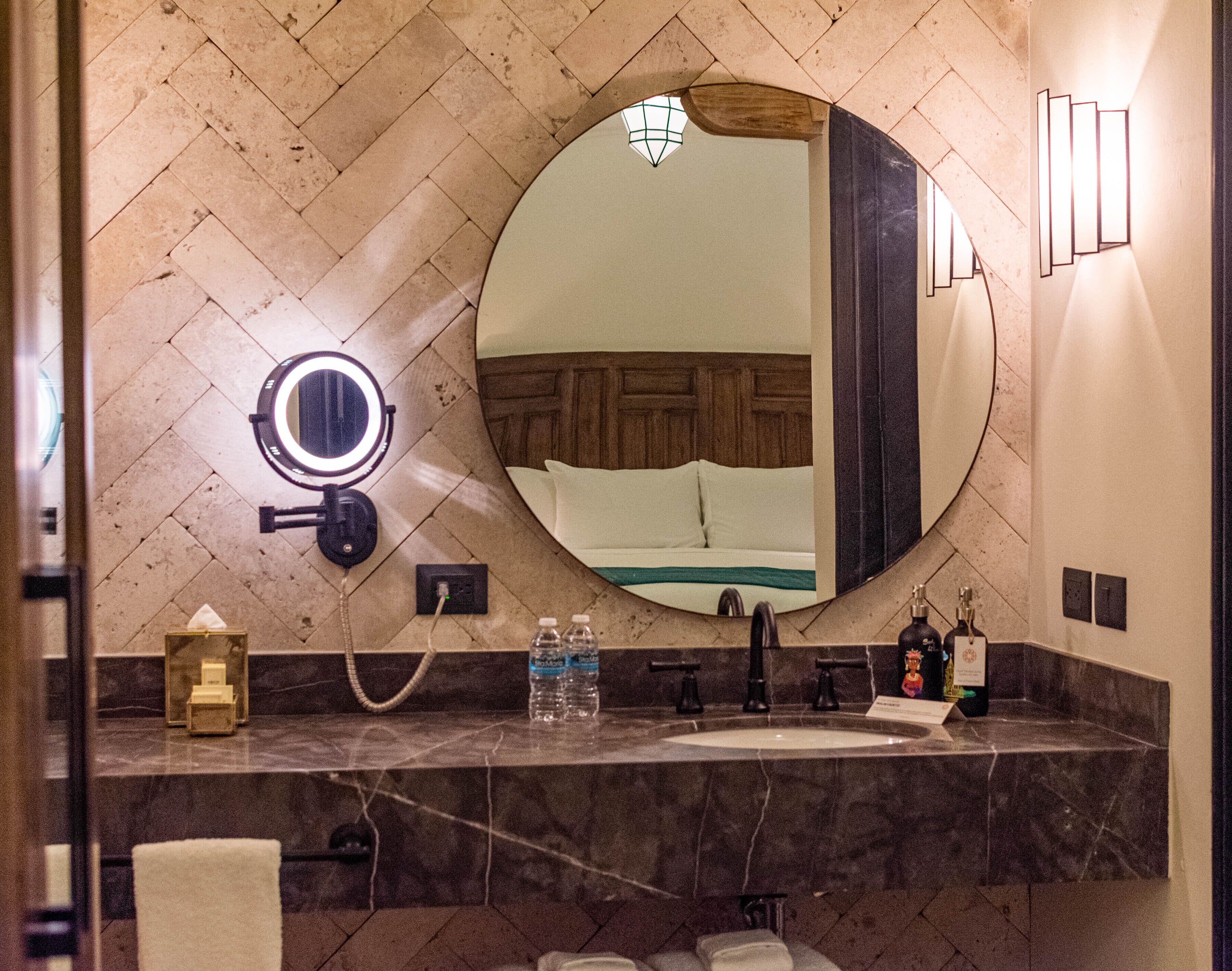 A bathroom with a round mirror, a vanity with a sink, and a towel rack.