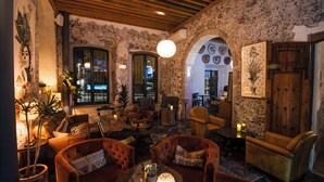 A cozy, rustic interior with stone walls, wooden beams, and leather furniture. There are multiple seating areas with cushions and a table with a lamp. - Casa 1810 Parque Hotel Boutique (San Miguel de Allende)