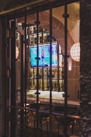 A bar area with a television screen displaying a program, bar stools, and a stone wall.