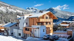 Een modern houten chalet met balkon, omringd door met sneeuw bedekte bergen.
