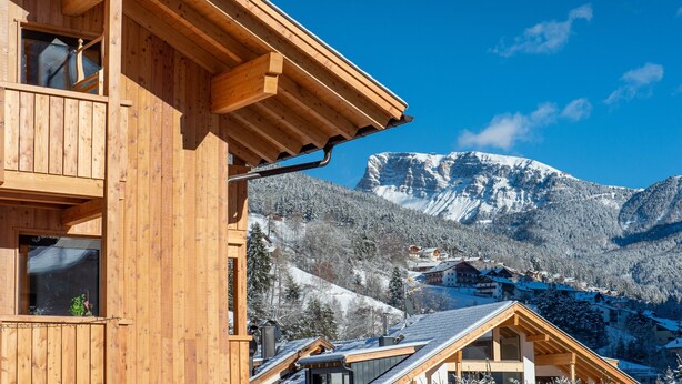 Een houten gebouw met balkon, uitzicht op een berg en besneeuwde bomen.