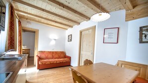 Een houten eettafel met stoelen, een houten plafond, een bank en een keuken met een spoelbak.