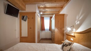 Een slaapkamer met een houten plafond, een bed met wit beddengoed, een nachtkastje met een lamp en een televisie aan de muur.