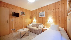 Ein Zimmer mit Holzvertäfelung, einem Sofa, einem Bett, einem Fernseher und zwei Wandleuchten.