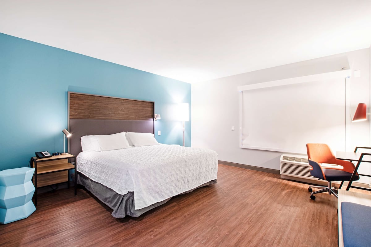 A modern hotel room with a wooden bed, a desk, a chair, and a large window.