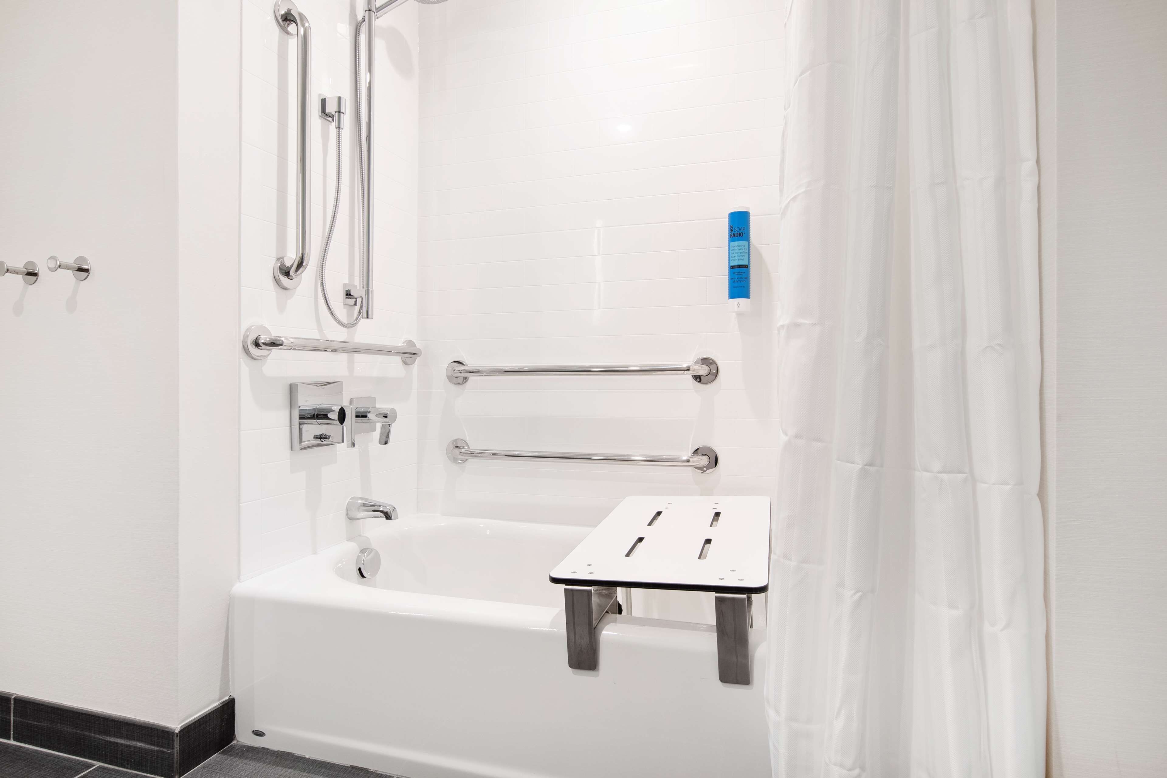 Un baño blanco con bañera, barras de apoyo y cabezal de ducha.