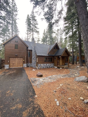A log cabin with a stone foundation, a garage, and a stone pathway leading to the entrance.