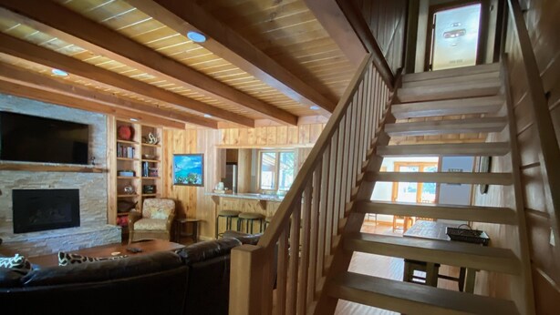 A wooden interior with a staircase, a kitchen area, and a seating area with a fireplace. - Classic Family Tahoe Cabin - West Shore Bliss! (Tahoma)