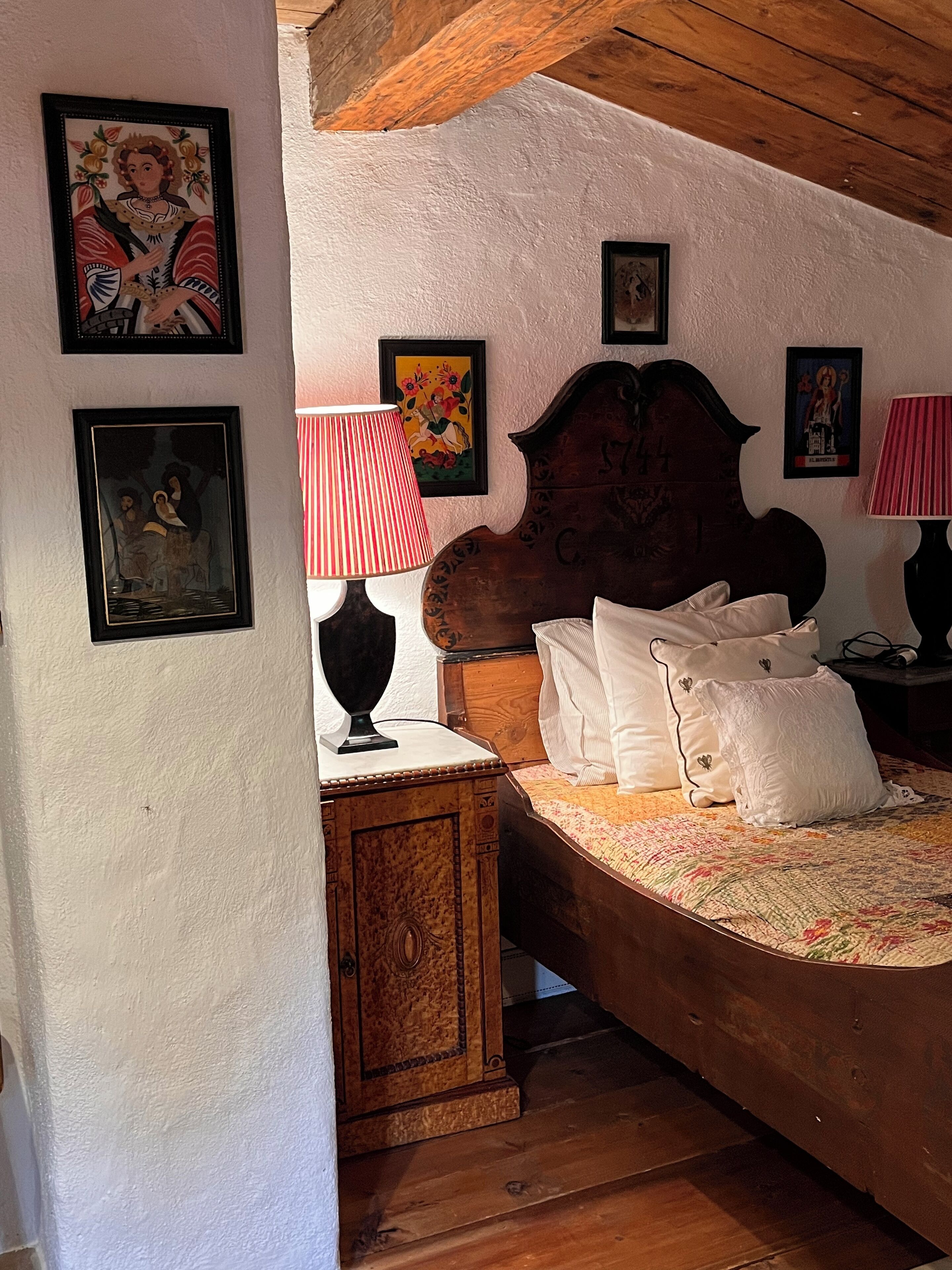 Un dormitorio con cabecera de madera, cama con almohadas blancas, mesita de noche de madera y una lámpara a rayas rojas y blancas. En las paredes hay cuadros enmarcados.
