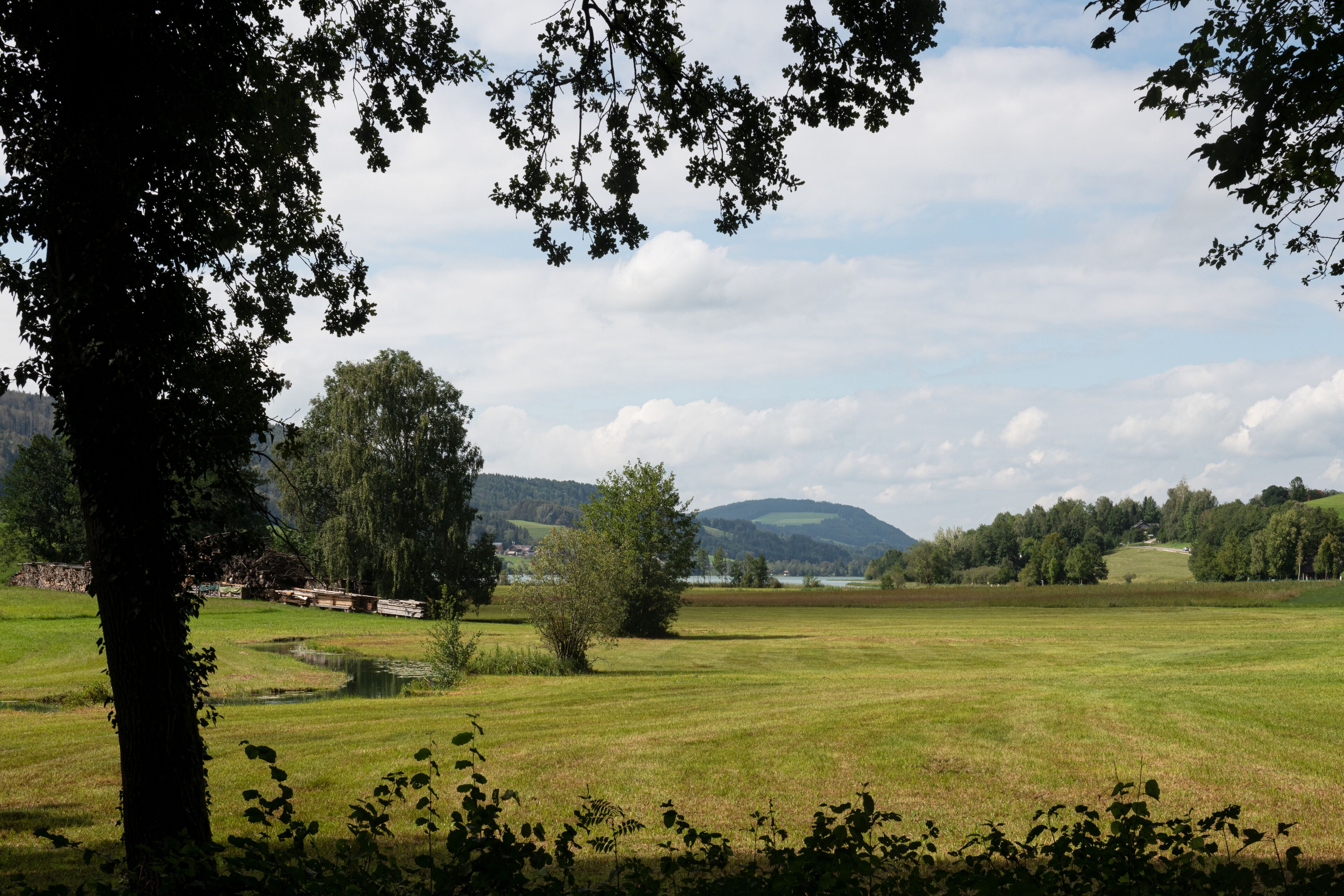 A rural landscape with a large open field, a pond, and distant hills.