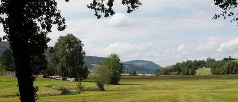 A rural landscape with a large open field, a pond, and distant hills.
