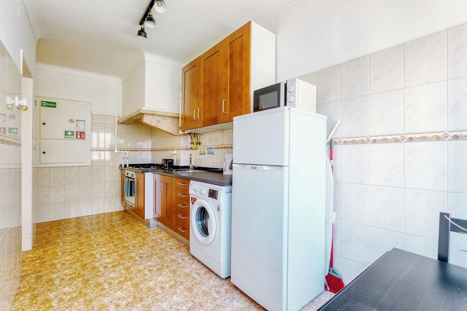 Eine kleine Küche mit Holzausstattung, einer Waschmaschine, einer Mikrowelle und einem Kühlschrank.
