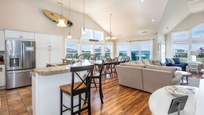 A spacious kitchen with a large island, wooden flooring, and a view of the outdoors through large windows. - Destination-OBX Soundfront, 8 bdrm, 10 bth, elavator, pool, hot tub, game room (Nags Head)