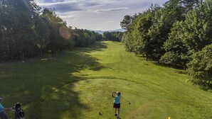 A golf course with a clear path, trees, and a person preparing to play.