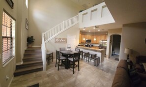 A spacious living area with a dining table, a kitchen with wooden cabinets, and a staircase leading to an upper level.