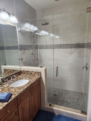 A modern bathroom with a granite countertop sink, a glass shower enclosure, and a tiled shower floor.