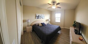 A bedroom with a bed, bedside tables, a ceiling fan, a window, and a TV on a stand.