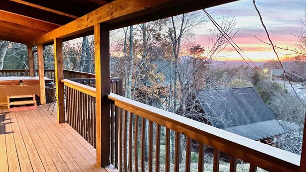 A wooden deck with a railing, a bench, and a view of trees and a house in the background. - NEW! Updated Family Log Cabin+Hot Tub+Pool Table! (Sevierville)